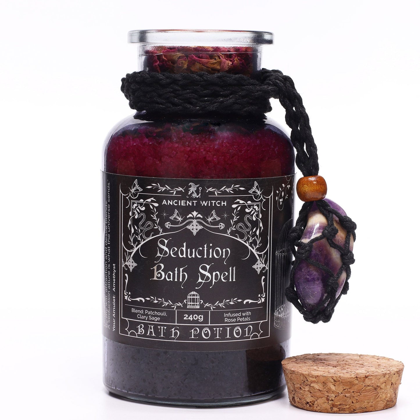 Glass bottle with cork lid off filled with Himalayan bath salts, rose petals and essential oils with an Amethyst crystal amulet