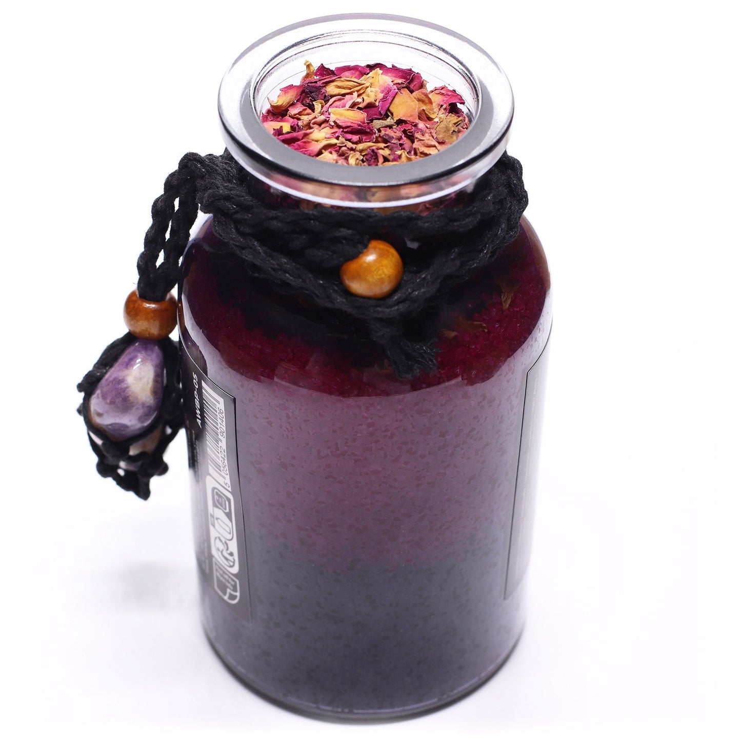 Glass bottle with cork lid off filled with Himalayan bath salts, rose petals and essential oils with an Amethyst crystal amulet from above